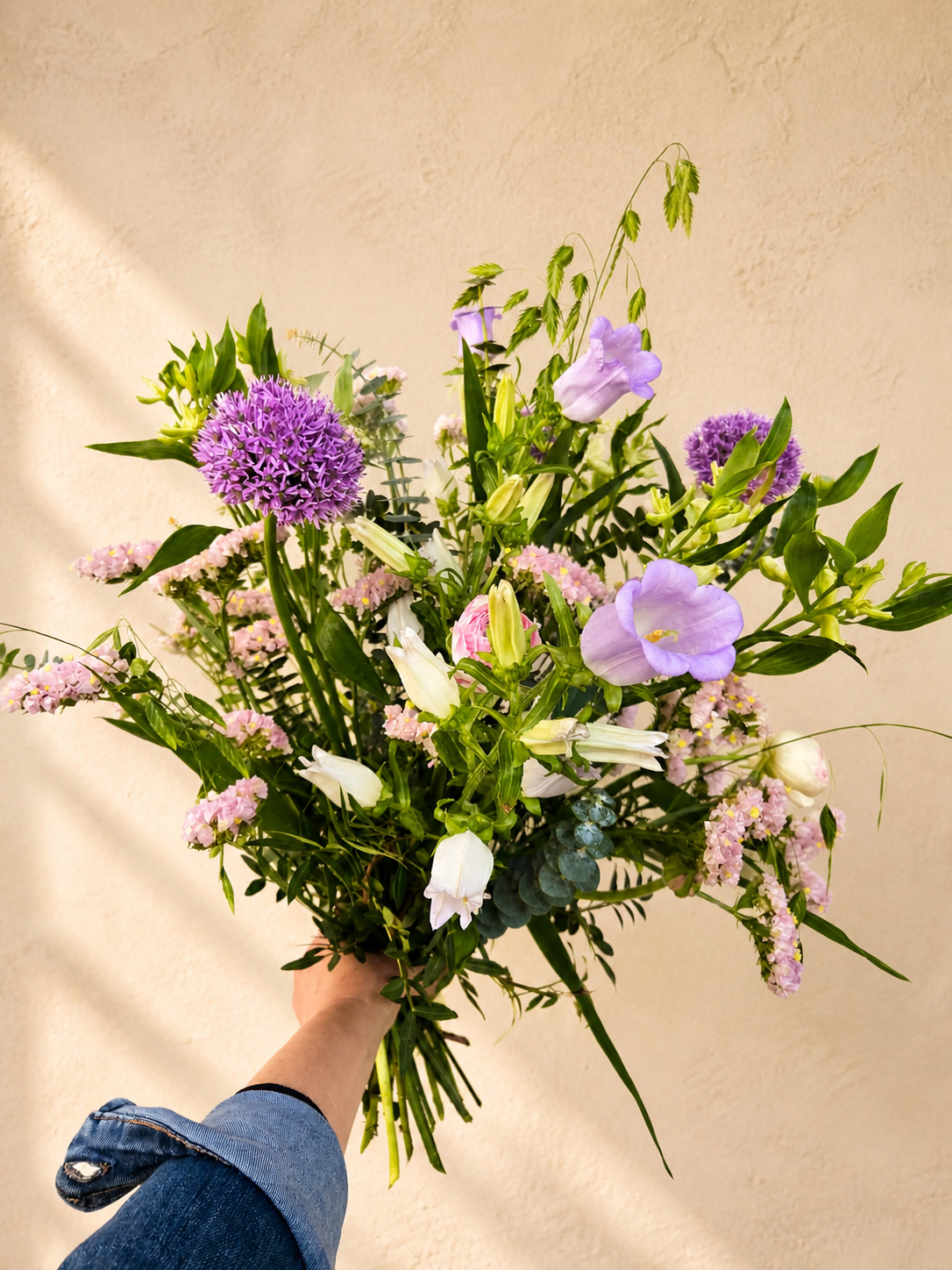 Luftig lilla buket med sæsonens friske blomster og grønt håndbundet af Iris Blomster.