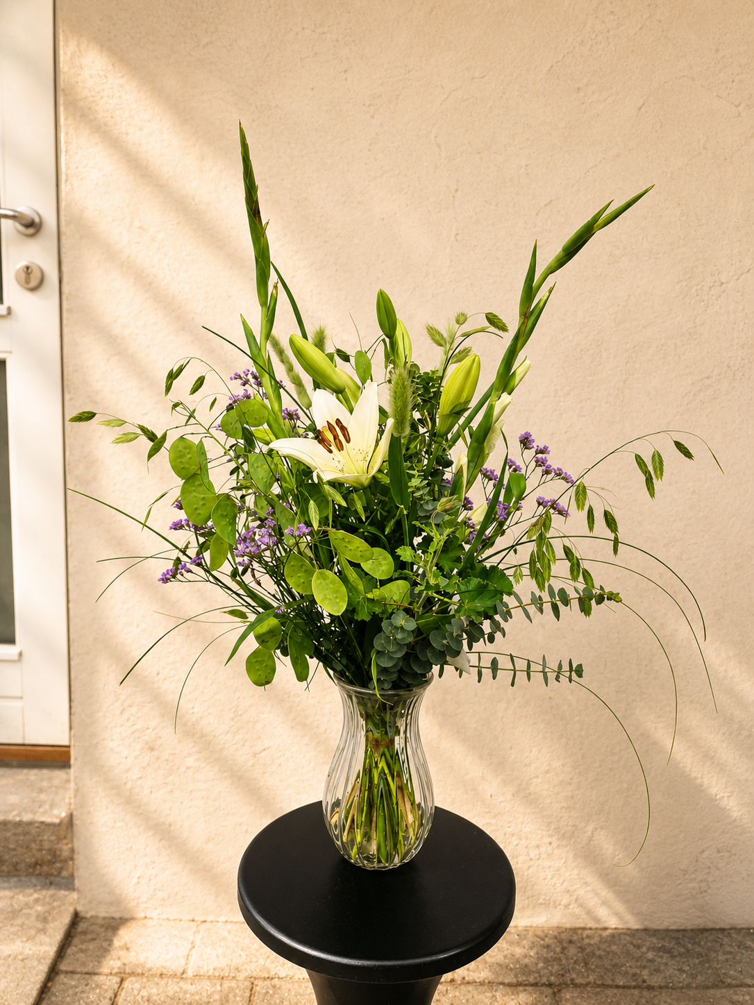 Høj og luftig buket med sæsonens blomster og grønt håndbundet af Iris Blomster.