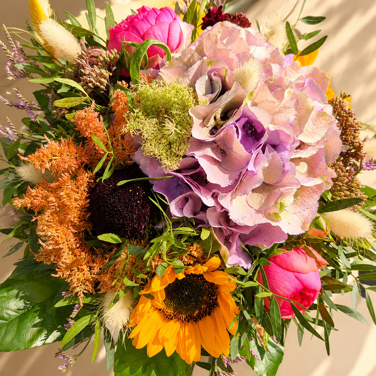 Tætbundet buket i lyse, grønne og varme sommernuancer. Buketten er bundet med årstidens friske blomster. 