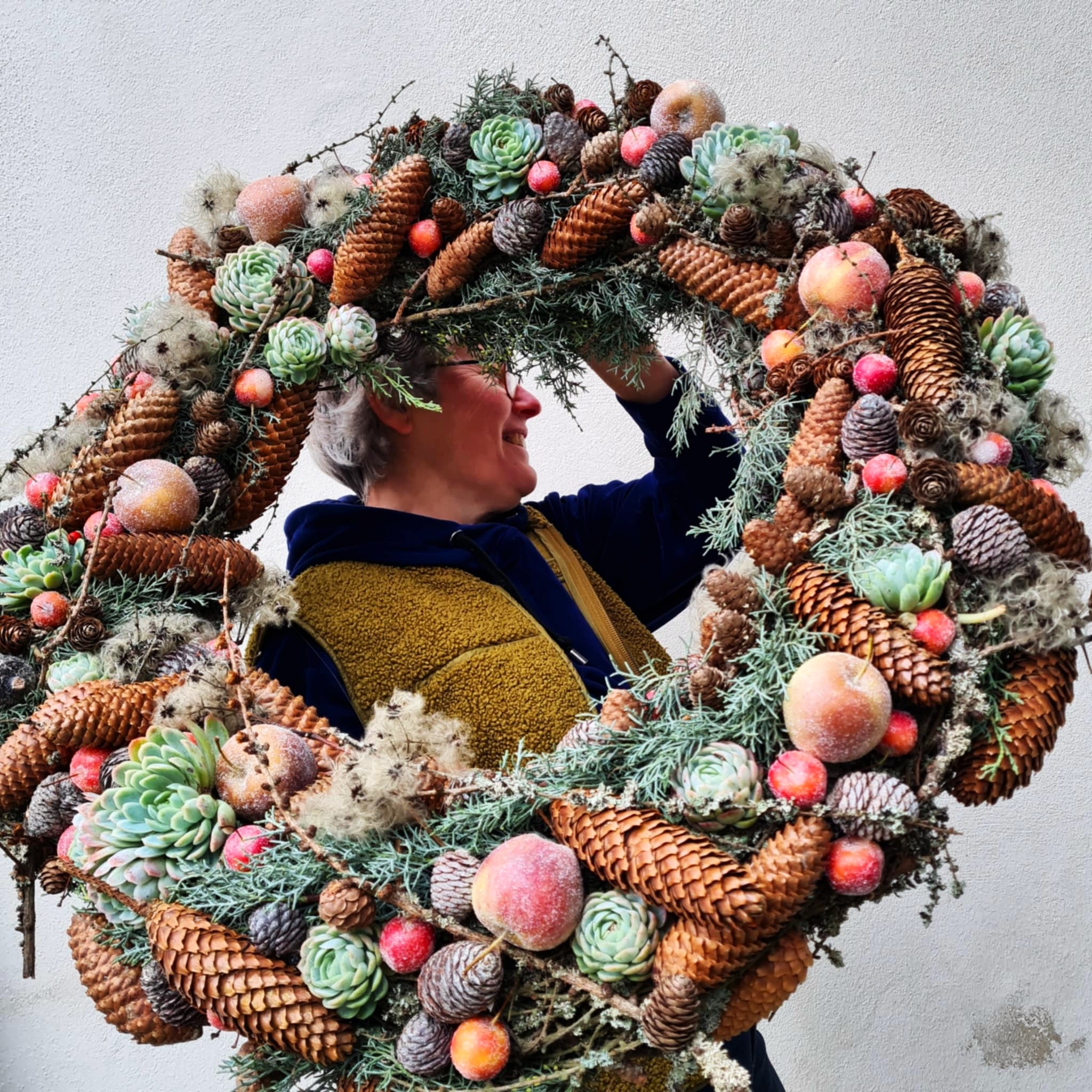 Indehaver Lene holder en stor julekrans lavet med mos, kogler, røde æbler, husløg og bær. 