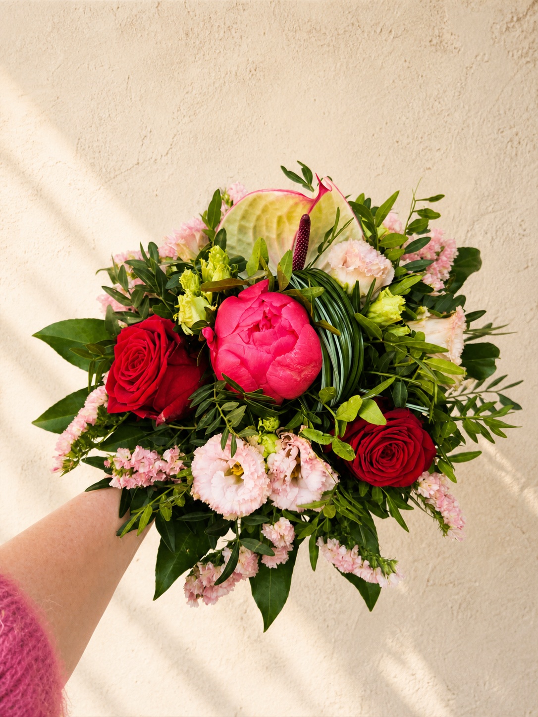 Tætbundet buket i lyse, grønne og røde nuancer. Buketten er bundet med årstidens friske blomster. 