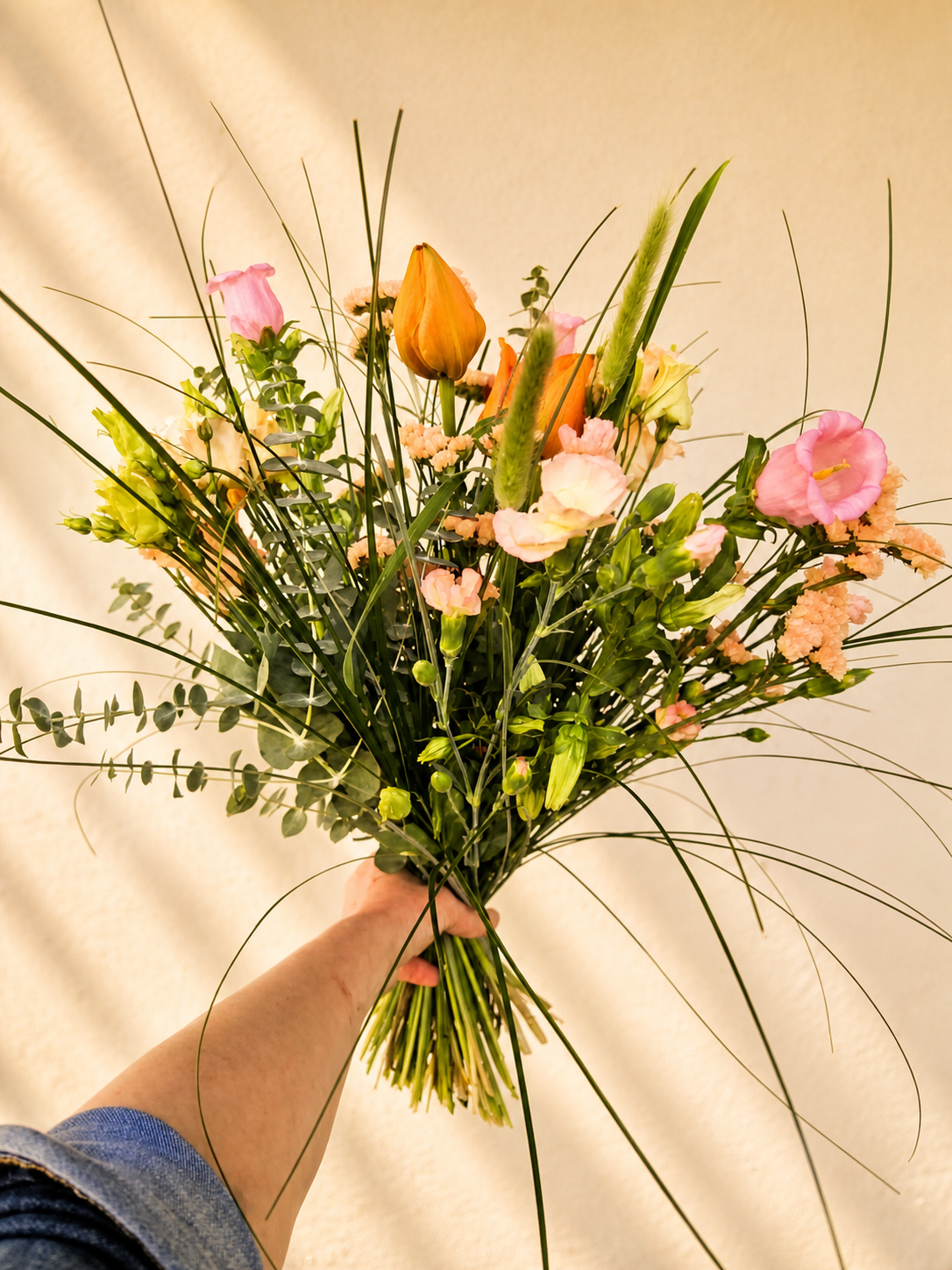 Luftig multifarvet buket med sæsonens friske blomster og grønne detaljer håndbundet af Iris Blomster.