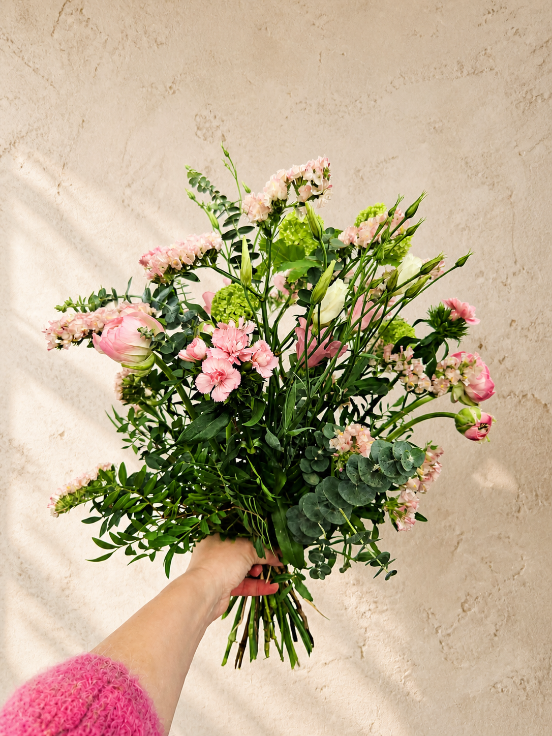 Lyserød håndbundet buket med sæsonens friske blomster og grønt i naturligt og let udtryk.